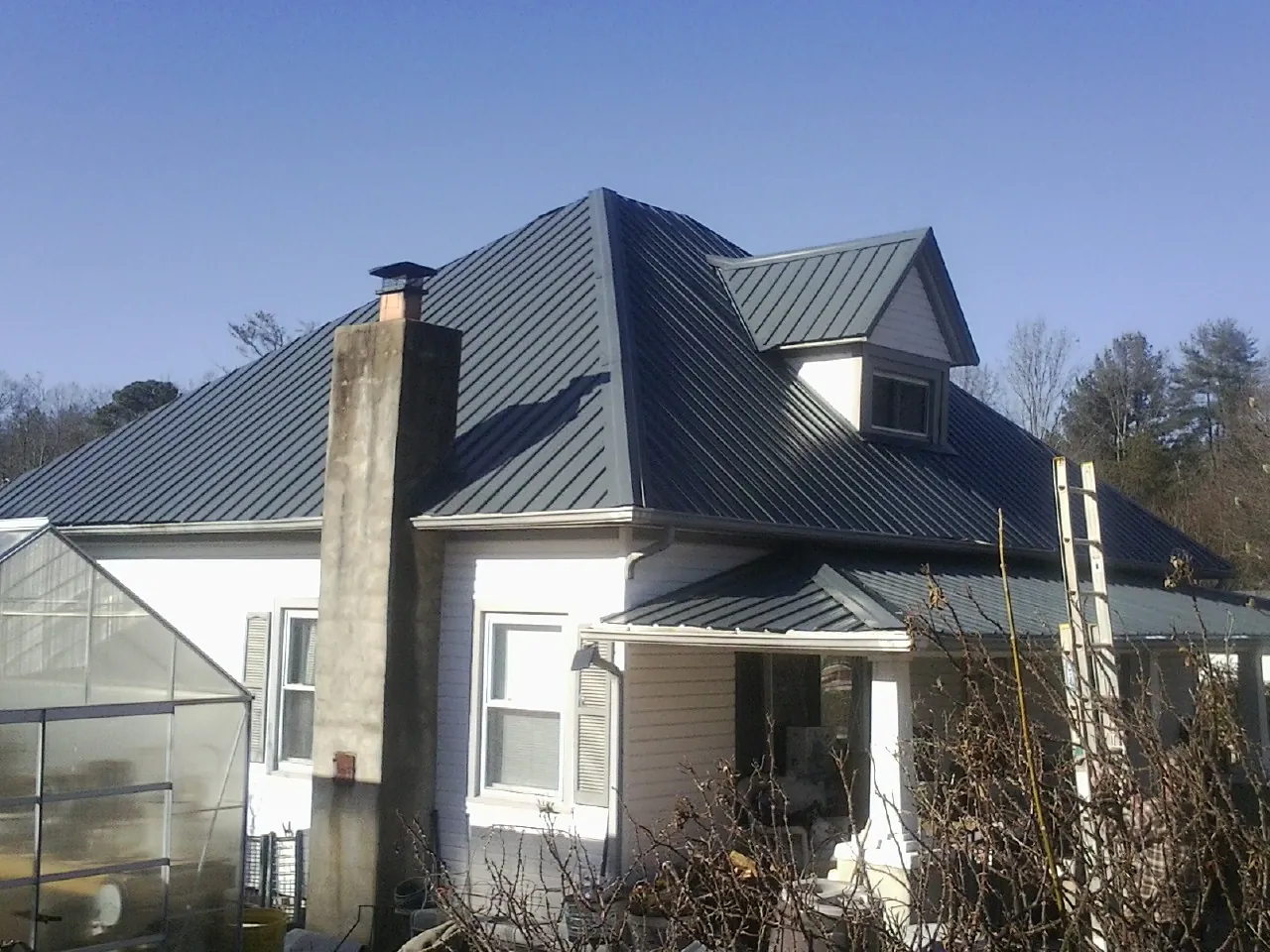 Dark blue standing seam metal roof on a white farmhouse with dormer — Slate & Tile Roof Repair by Roofing Brothers in Powhatan