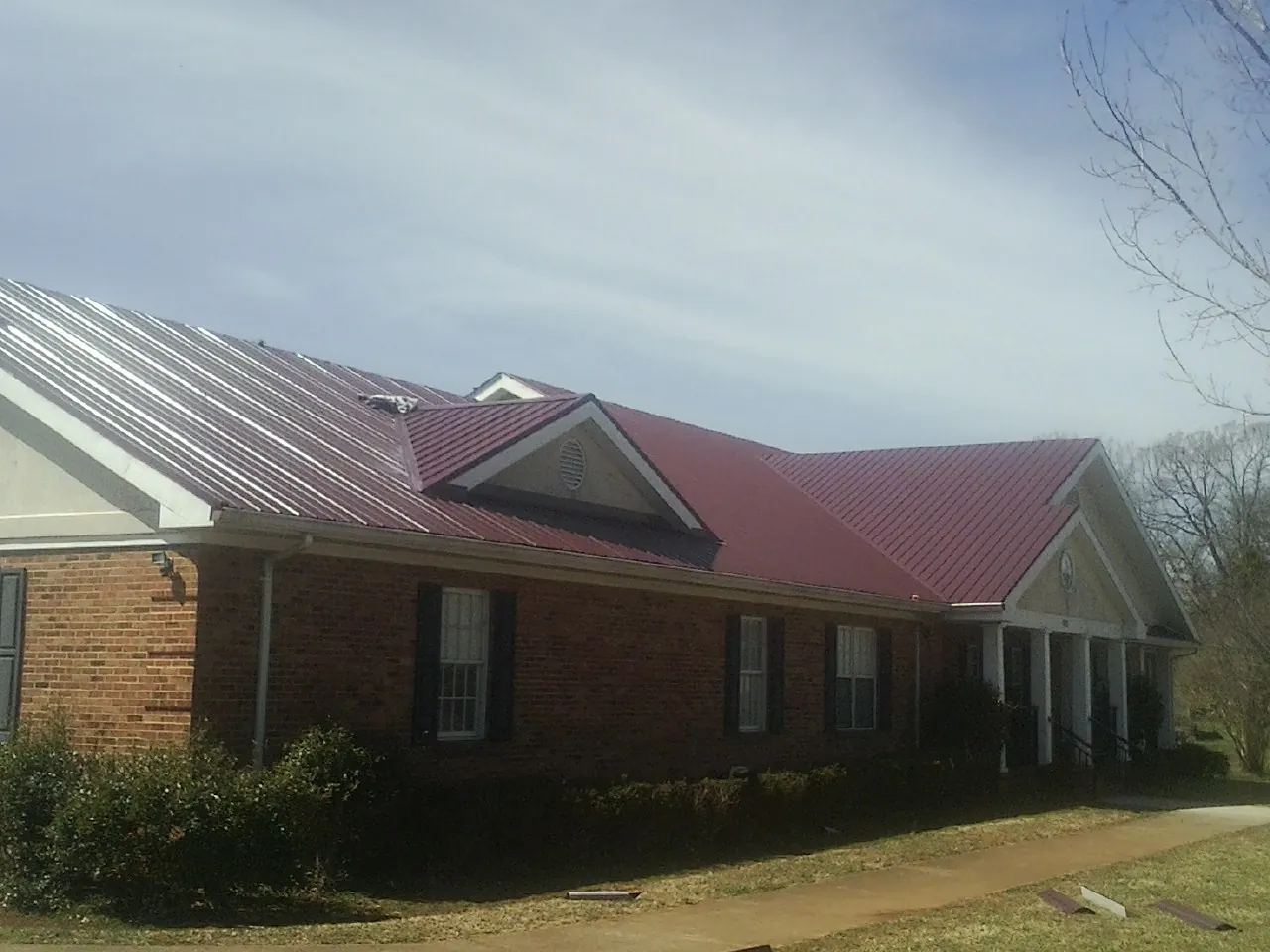Red metal roof with gabled entries on a long brick building, from a Hail Damage Roof Repair job in Powhatan