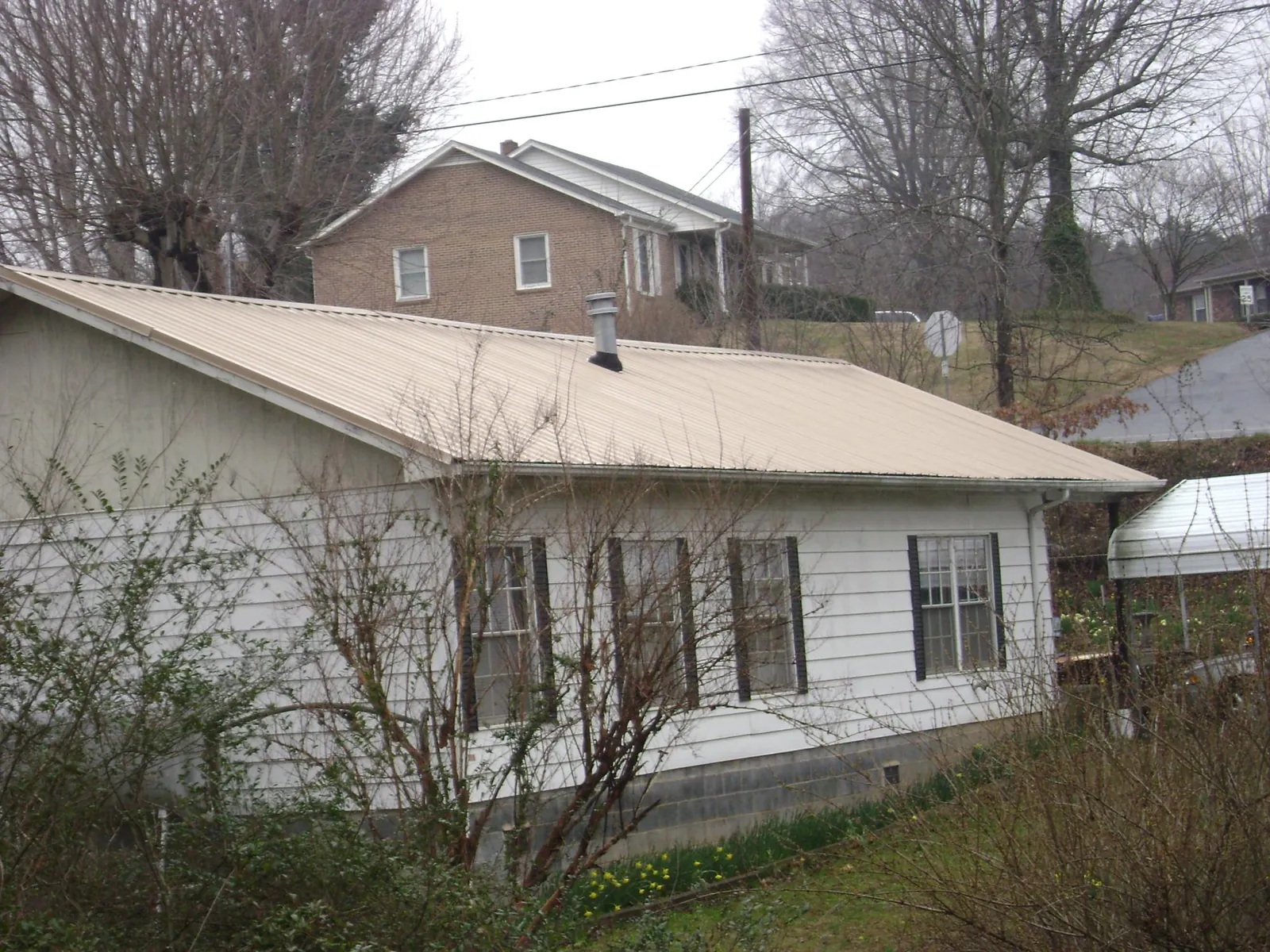 Tan metal roof on a white sided house set into a hillside — Commercial Roofing by Roofing Brothers in Powhatan
